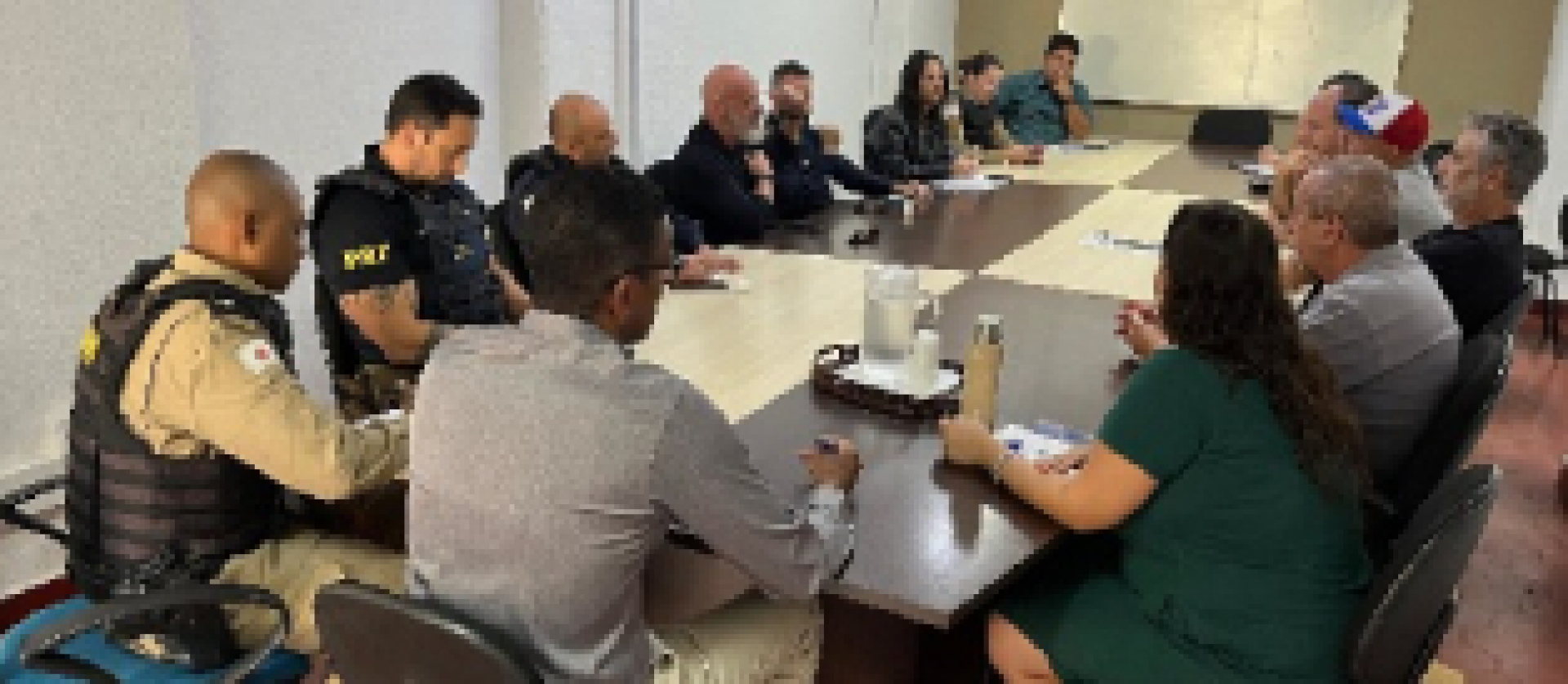 Reunião com participação de policiais e civis discutindo assuntos em uma sala de conferência.