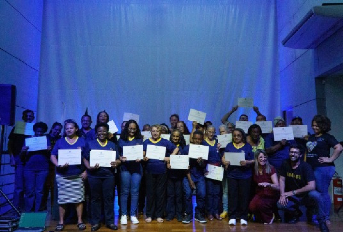 Grupo de pessoas posa em um palco exibindo certificados de conclusão.