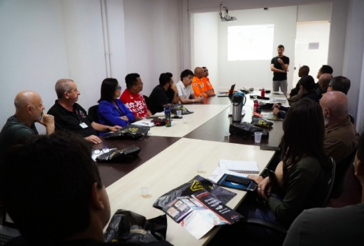 Pessoas participam de uma reunião ou treinamento em sala com apresentação projetada na parede.