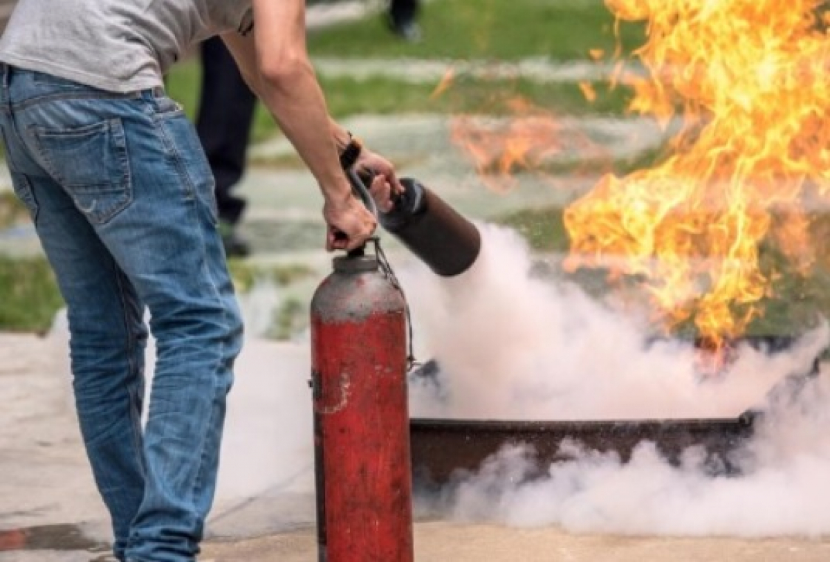 Pessoa participa de simulação de combate a incêndio utilizando extintor em ambiente ao ar livre.