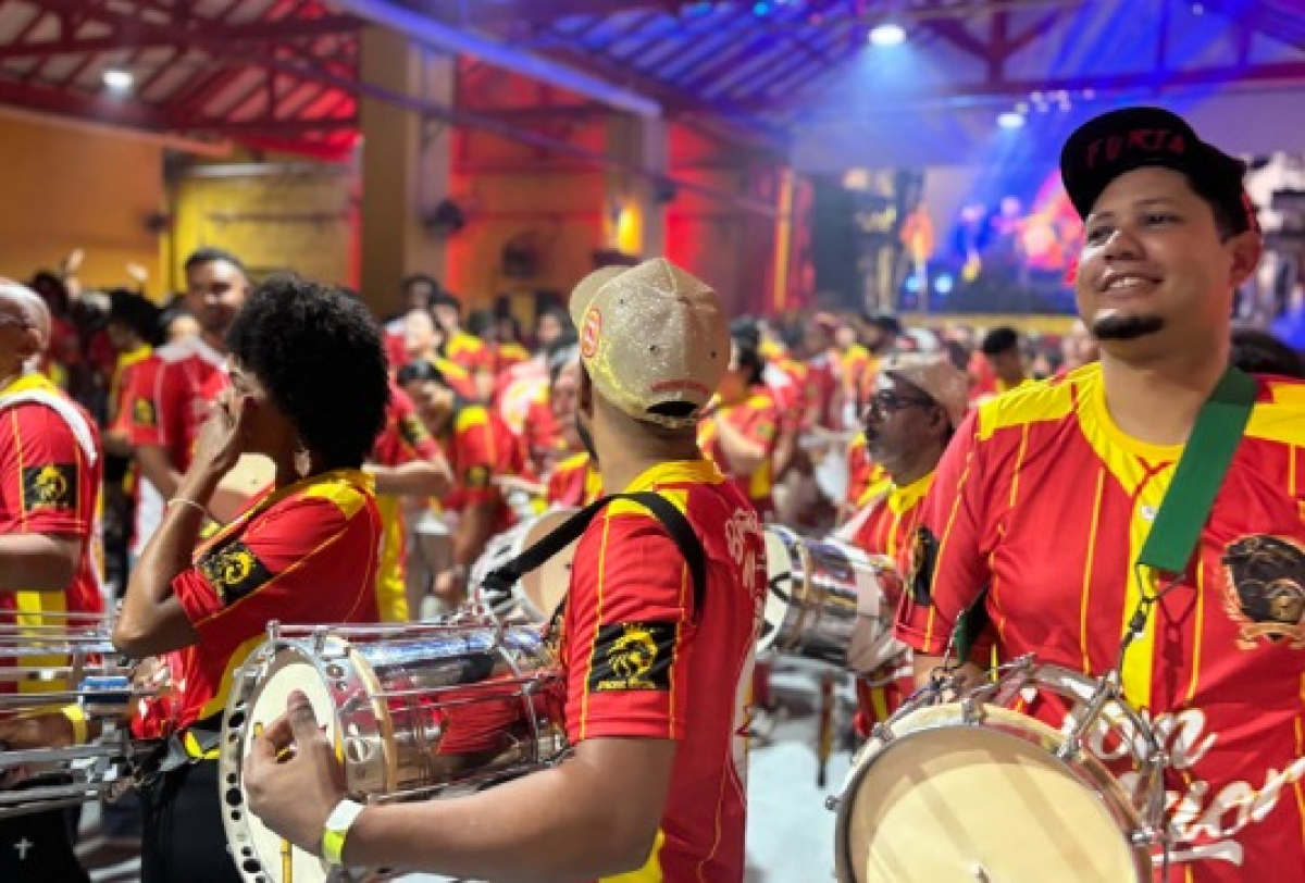 Ritmistas animam o ensaio de escola de samba com instrumentos de percussão e clima festivo.