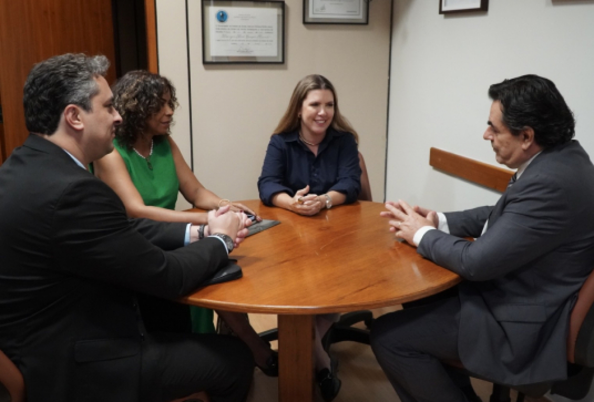 A imagem mostra quatro pessoas sentadas ao redor de uma mesa redonda em um escritório, discutindo. 