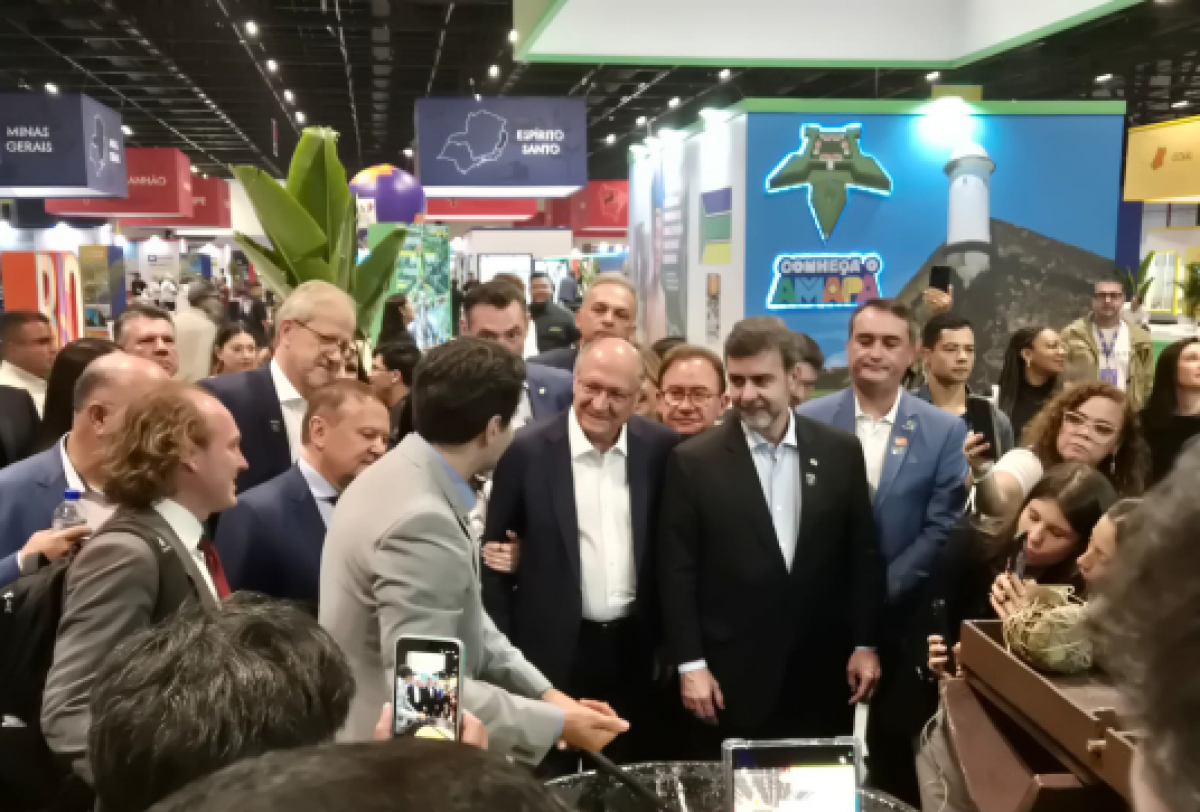 Grupo de autoridades e visitantes reunidos em um estande de feira ou evento com foco em estados brasileiros.