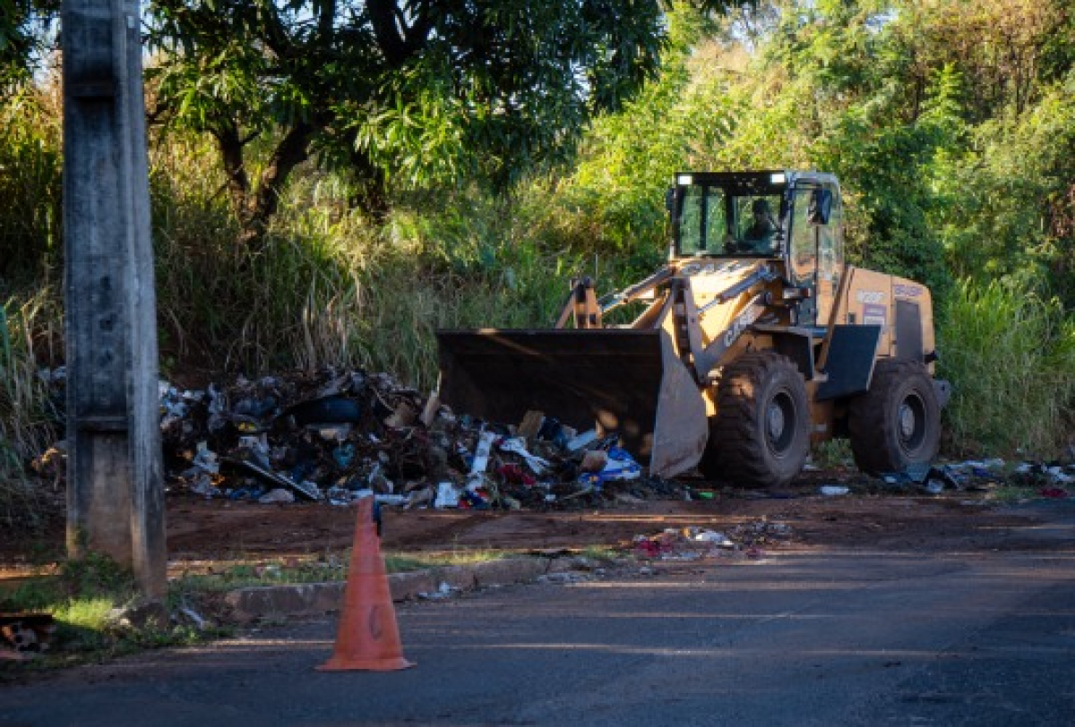 Retroescavadeira realizando a limpeza e remoção de lixo acumulado às margens de uma via.