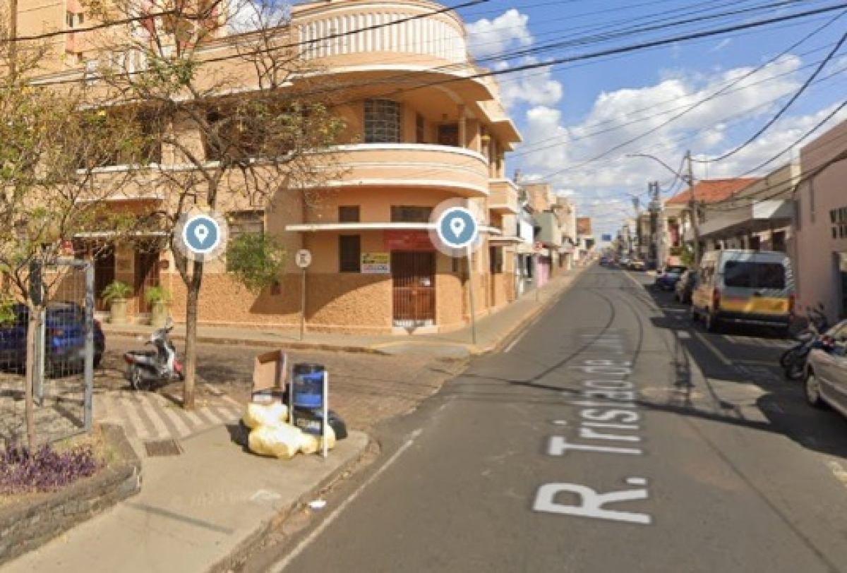 Esquina urbana na Rua Tristão de Castro com prédio antigo, lixeira cheia e trânsito leve.