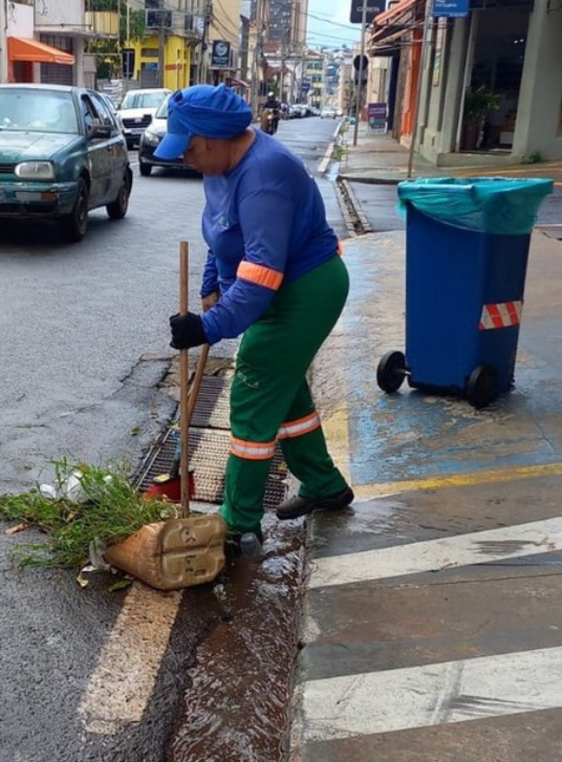 Funcionária da limpeza urbana varre folhas e sujeira de uma sarjeta em uma rua da cidade.