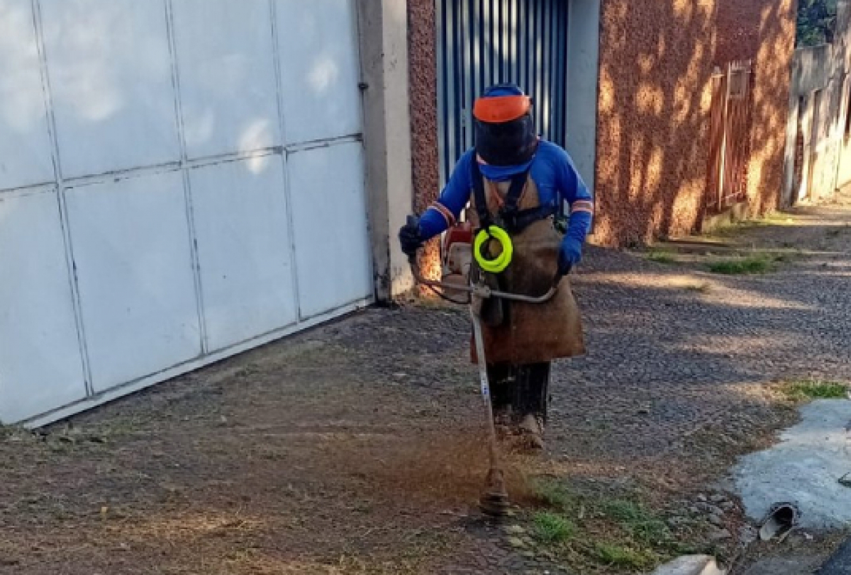 Trabalhador realiza serviço de roçagem em calçada para limpeza e manutenção urbana. 