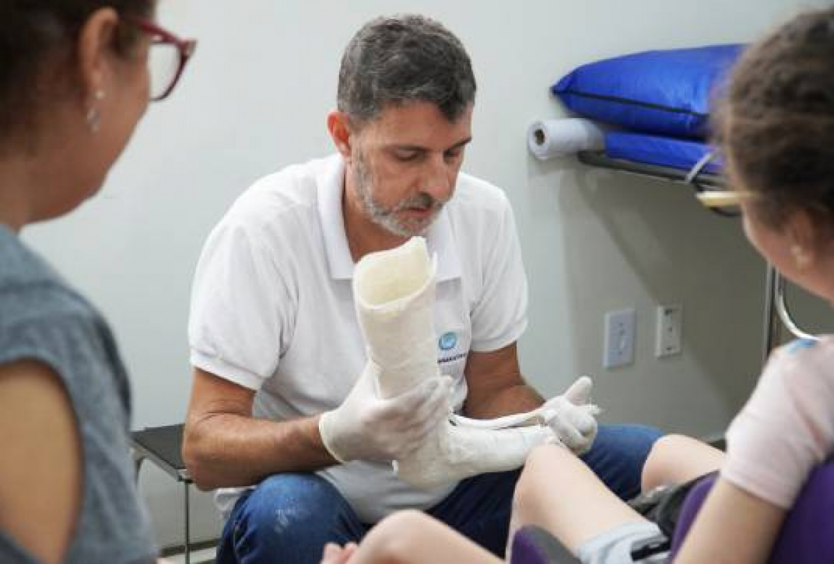 Profissional de saúde ajusta uma órtese ou prótese na perna de uma criança em ambiente clínico.    