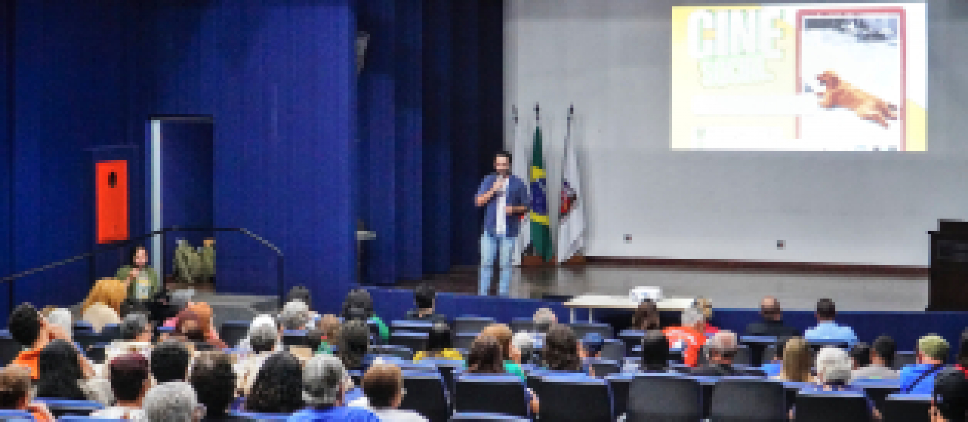Público assiste a uma apresentação no auditório com projeção e palestra.