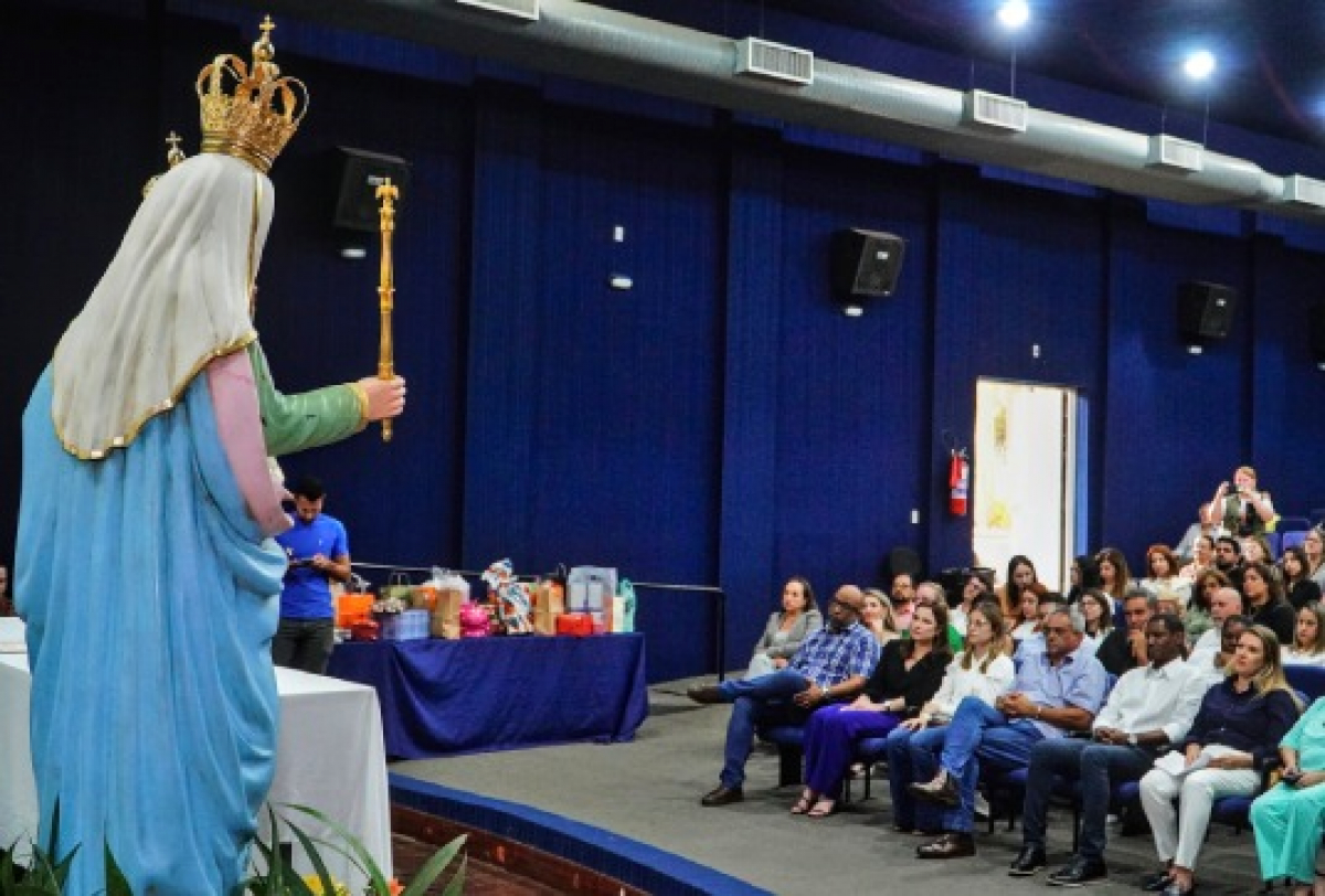 Evento religioso em auditório com público atento e estátua de Nossa Senhora em destaque.
