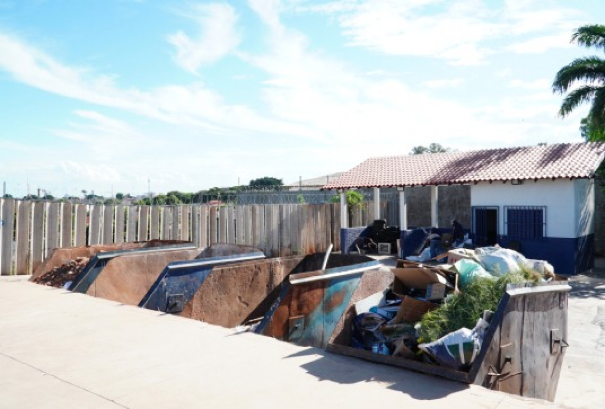 Área externa com contêineres de lixo e materiais descartados, ao lado de uma residência.