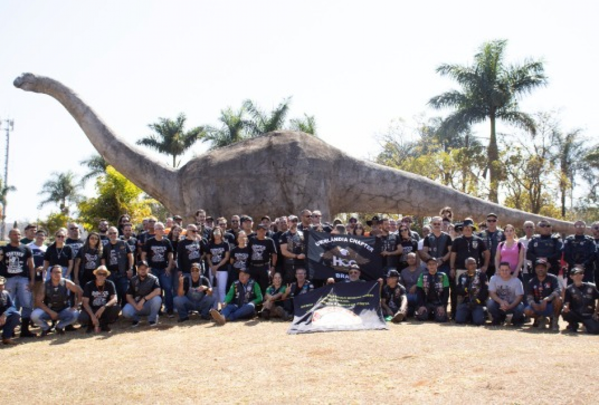 Grupo do HOG Americana Chapter posa em frente a uma estátua de dinossauro em um parque temático.