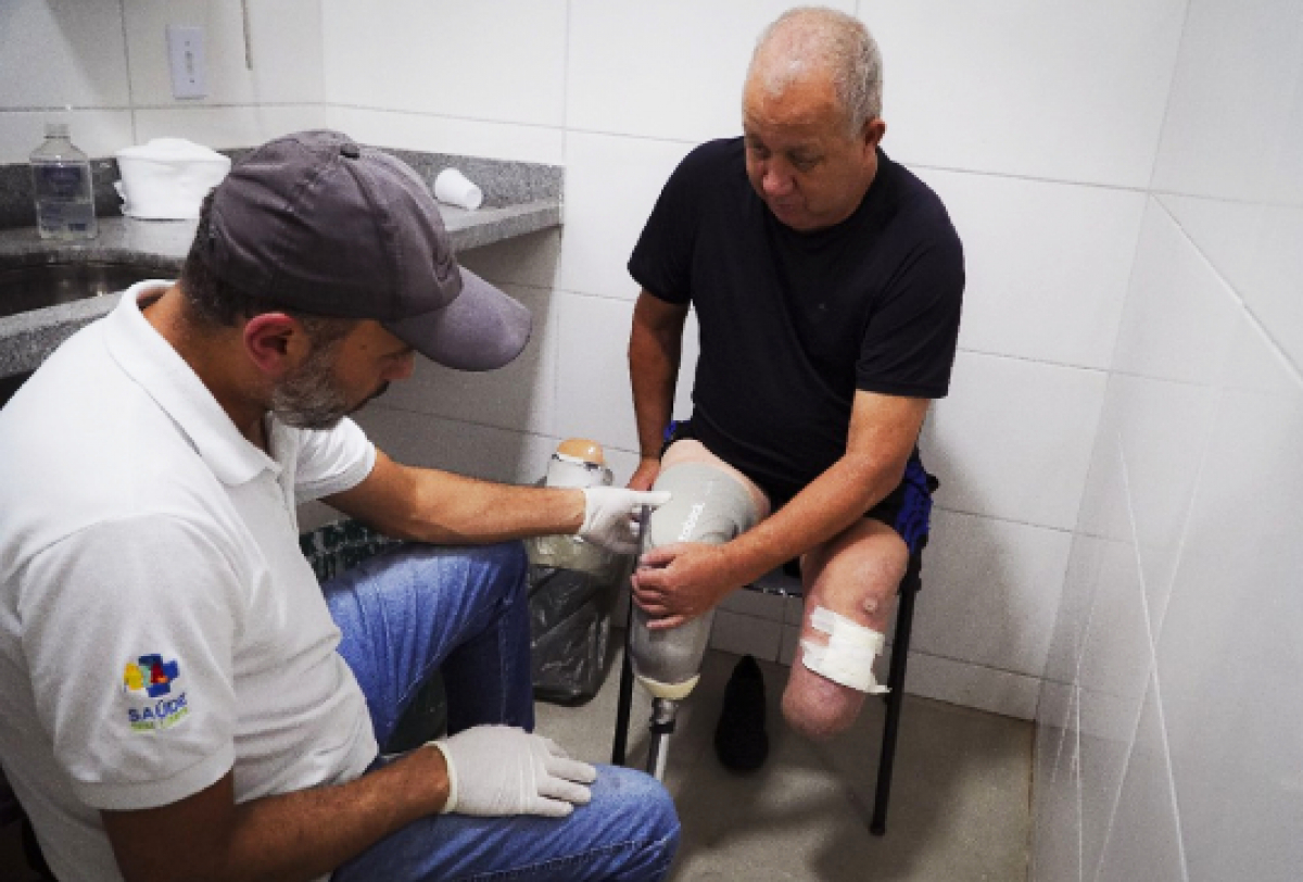 Profissional de saúde auxilia paciente com prótese na perna durante atendimento em ambiente clínico.