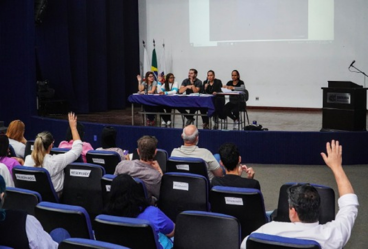 Audiência em auditório reúne participantes com interação entre público e mesa diretora.