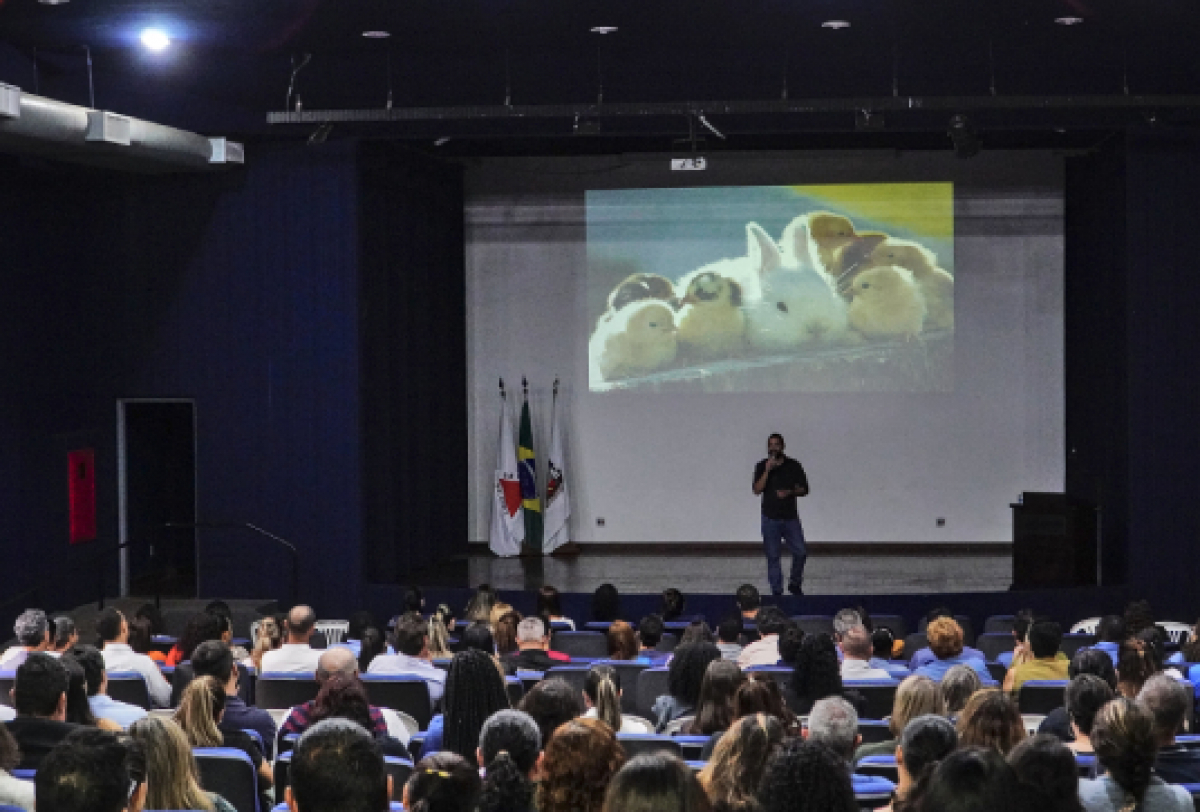 Palestra em auditório com público atento e imagem de filhotes projetada no telão.