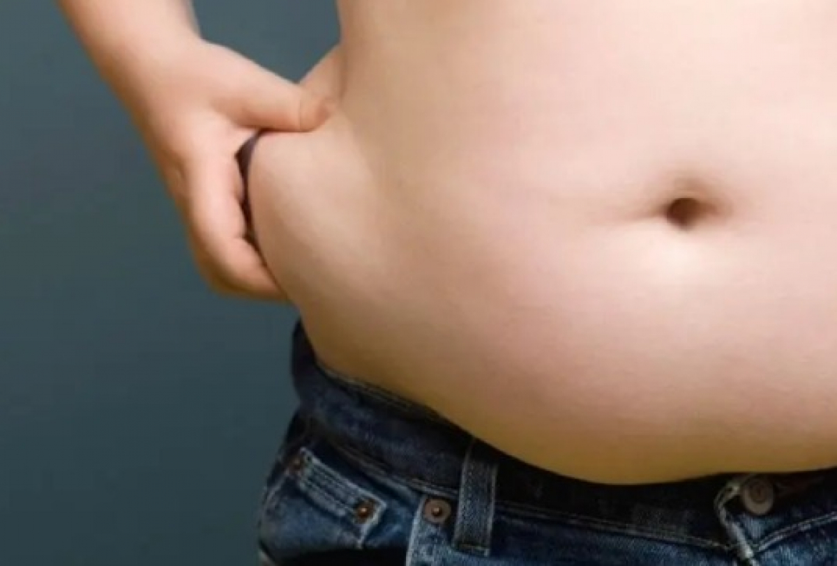 Imagem mostra o abdômen de uma pessoa usando calça jeans, enquanto aperta a pele lateral da barriga com a mão.