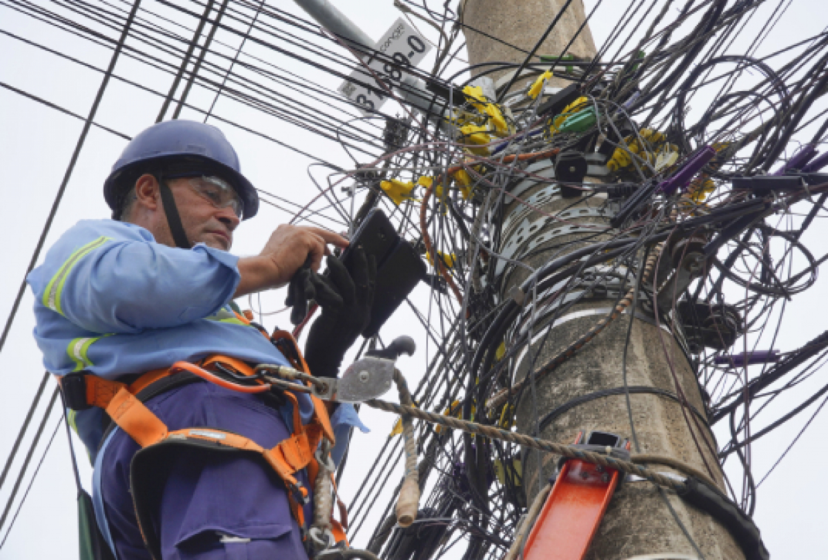 Técnico de manutenção trabalhando em um poste com fios elétricos emaranhados.