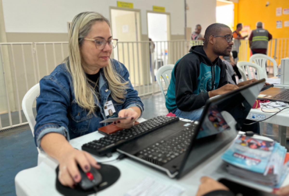 Atendentes trabalham em computadores em um ambiente de atendimento ao público.