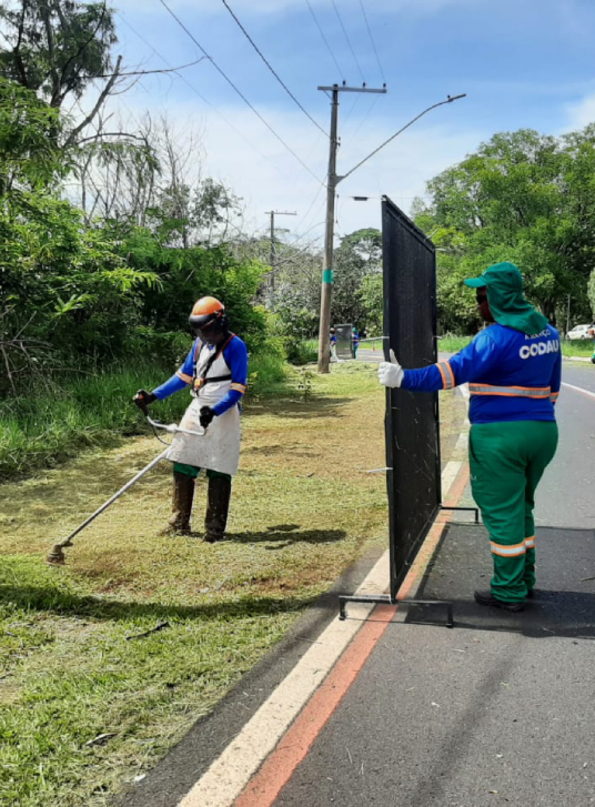 Trabalhadores da CODAU fazem a manutenção da beira de uma avenida.