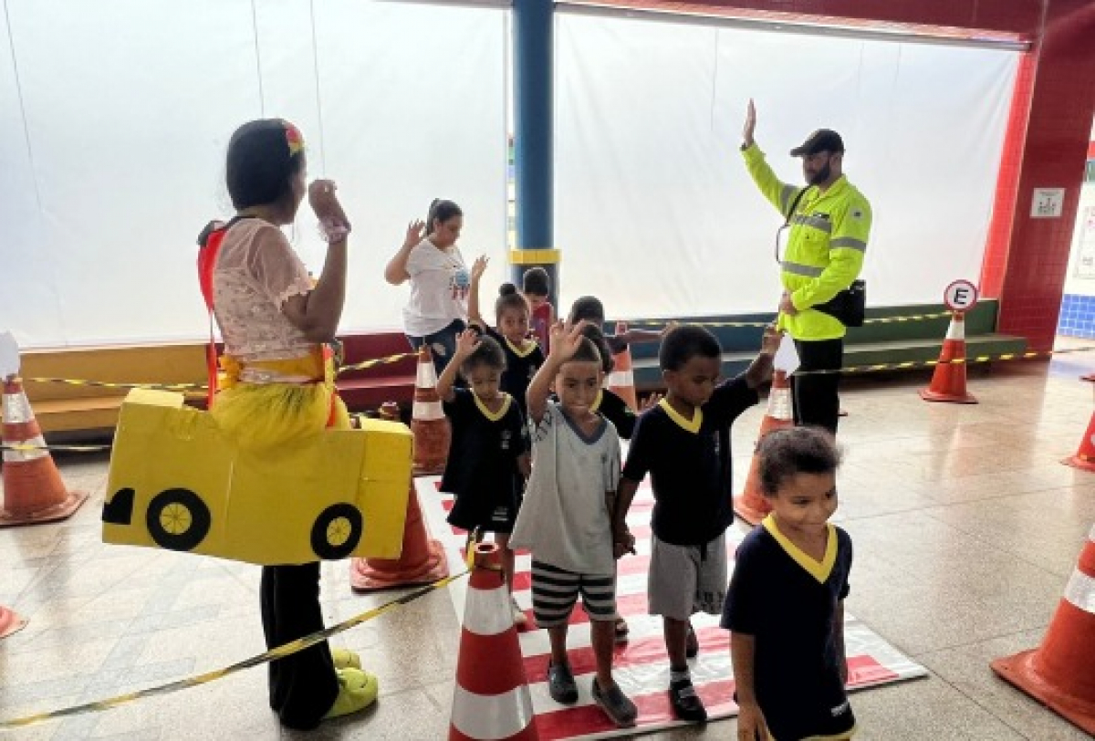 A imagem mostra uma atividade educativa com crianças aprendendo sobre segurança no trânsito.