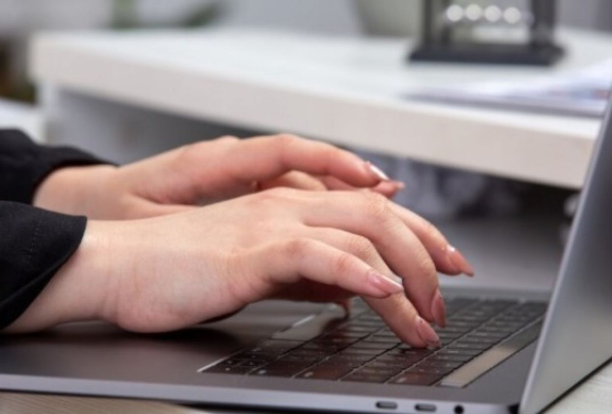 A imagem mostra uma pessoa digitando em um laptop, com foco nas mãos sobre o teclado.