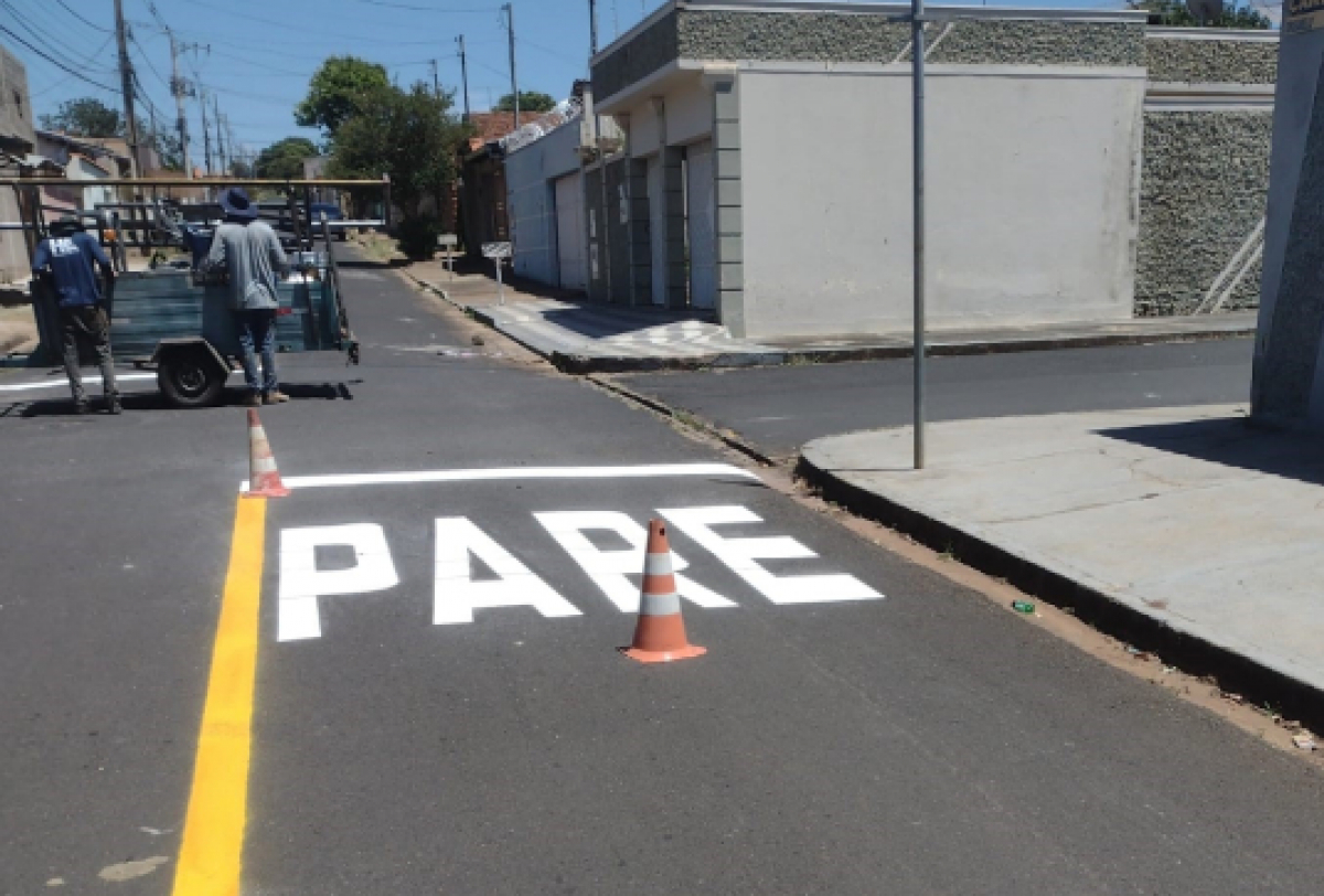 Pintura de sinalização viária com a palavra PARE em uma rua residencial.