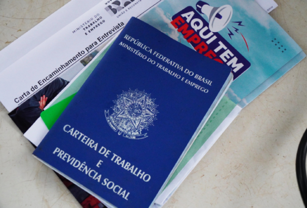 A imagem mostra uma Carteira de Trabalho e Previdência Social do Brasil, junto a documentos relacionados a emprego e encaminhamento para entrevista.