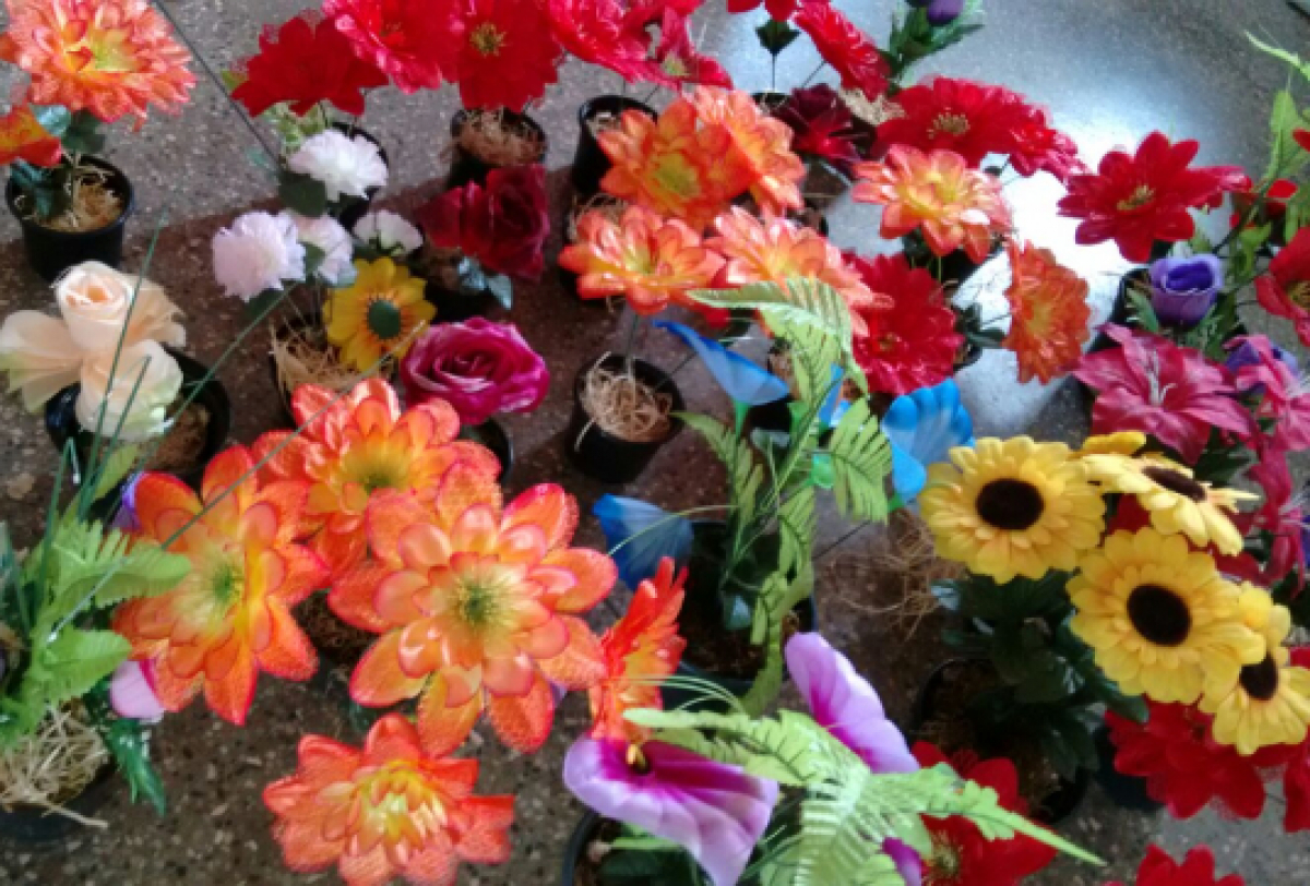 Arranjos de flores artificiais coloridas em pequenos vasos, organizados para exposição ou decoração.