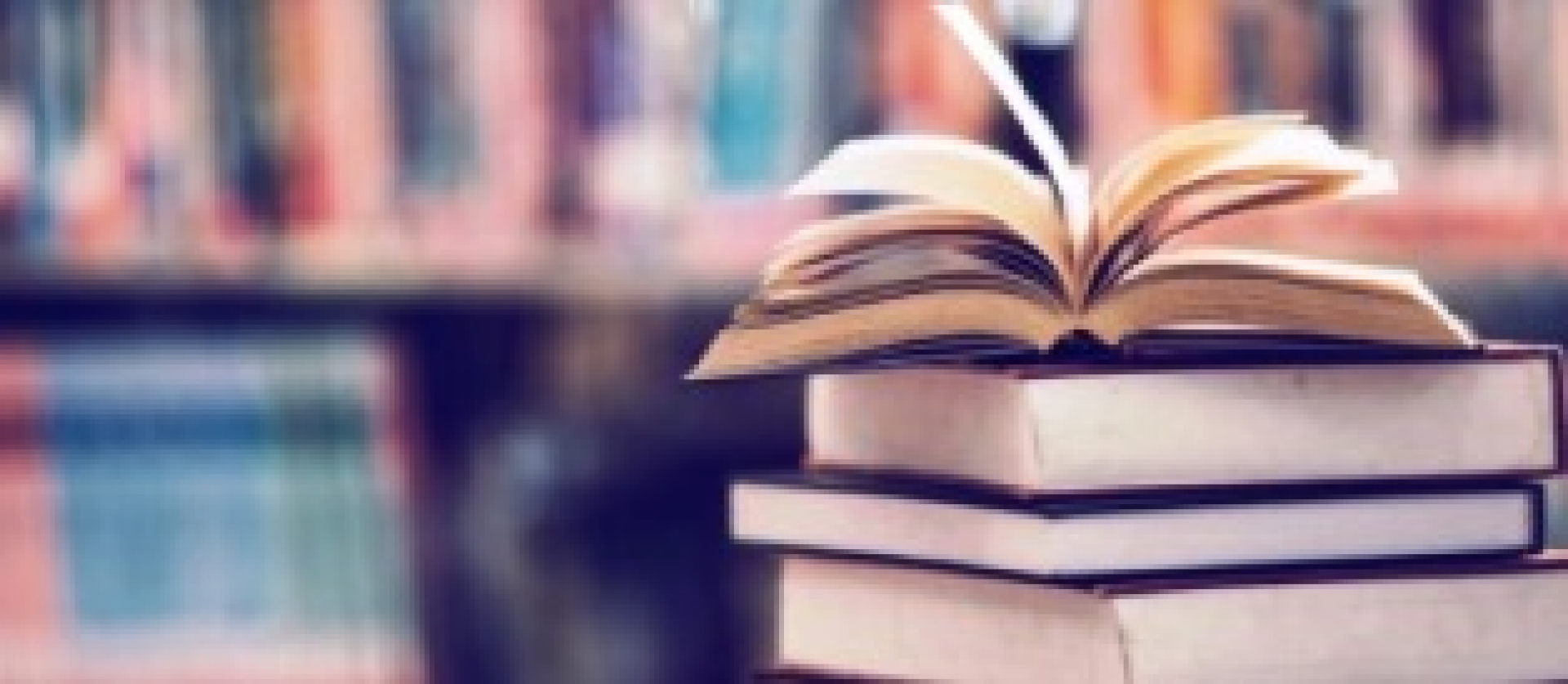 Livro aberto sobre uma pilha em uma biblioteca, destacando o ambiente de leitura e conhecimento.