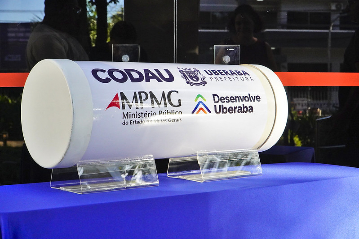 Cápsula com logotipos de órgãos públicos e instituições parceiras de Uberaba, exposta sobre uma mesa azul.