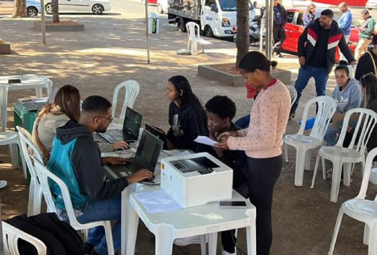Atendimento comunitário ao ar livre com uso de computadores e impressora para auxiliar o público.