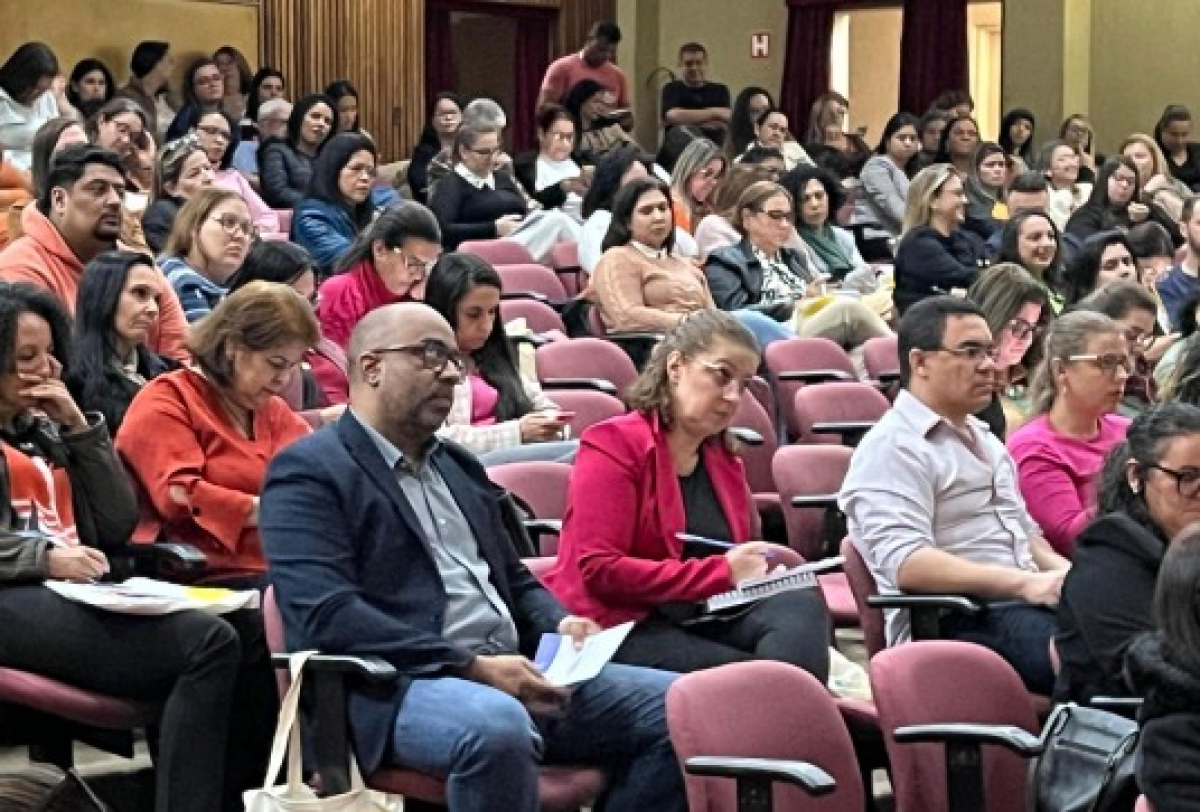 Pessoas participam atentas de uma palestra em um auditório lotado.