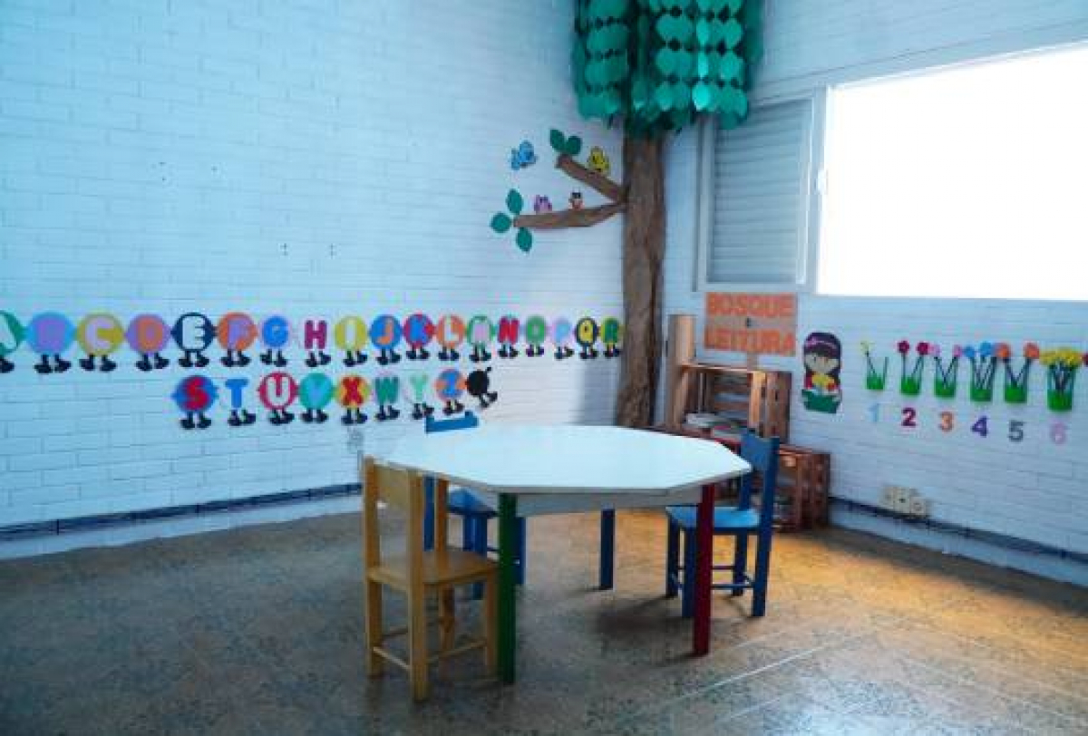A imagem mostra uma sala de aula ou cantinho de leitura alegremente decorado, projetado para crianças pequenas.