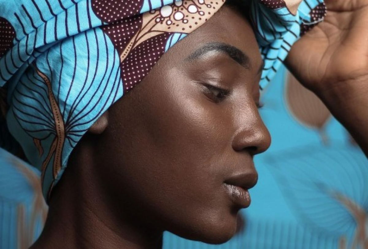 Mulher com turbante colorido posa em perfil, destacando beleza e cultura afrodescendente.
