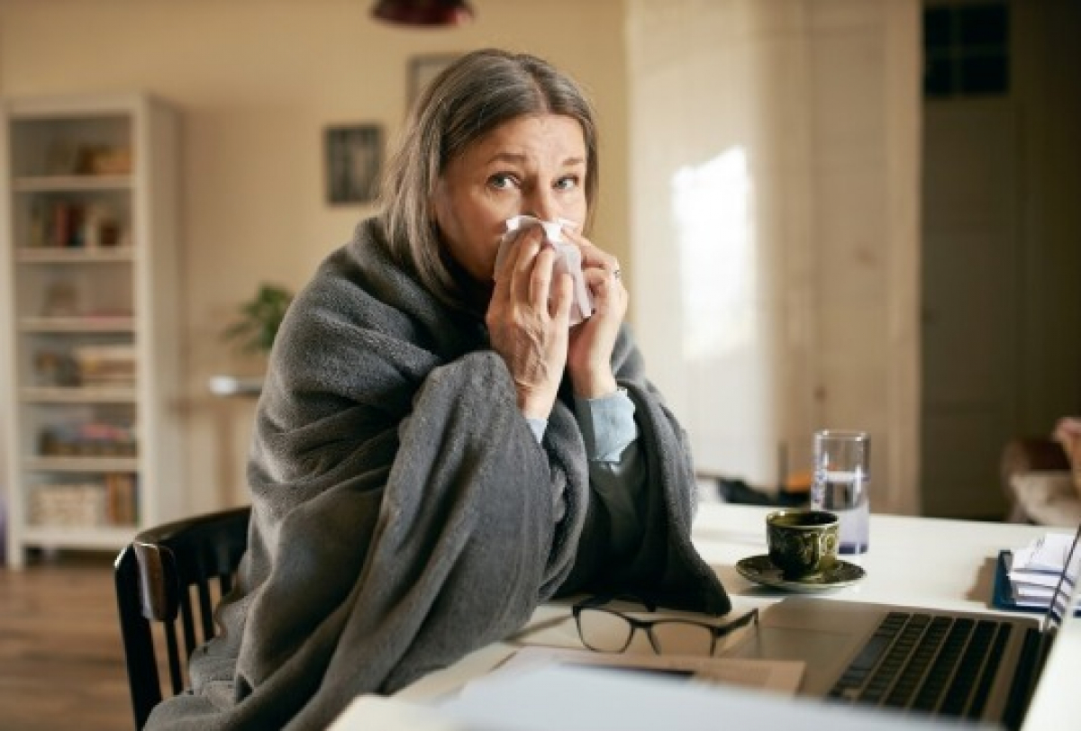 Mulher com sintomas de gripe em casa retrata os impactos das síndromes gripais no dia a dia.