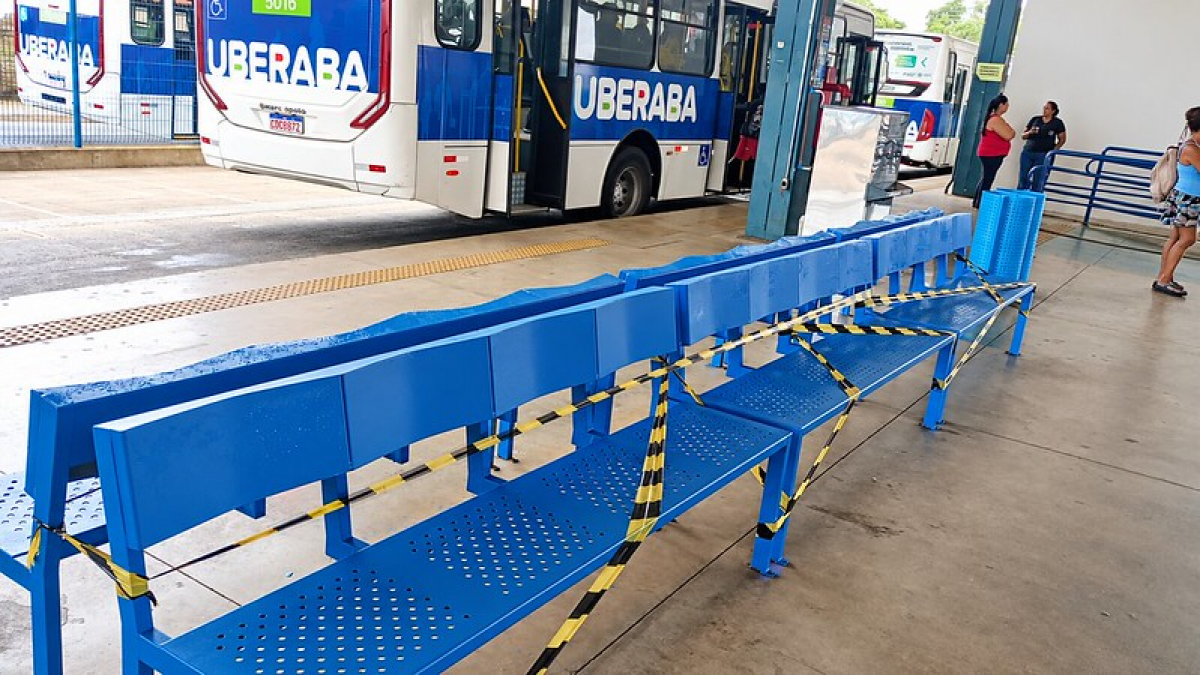 Bancos azuis interditados com fita de segurança aguardam manutenção em um terminal de ônibus de Uberaba.