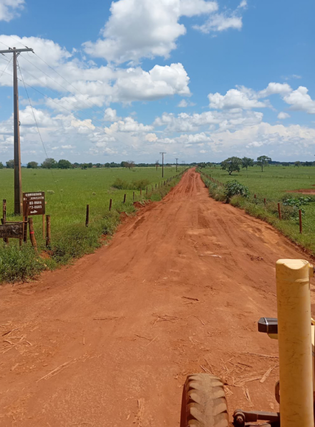 Uma estrada rural cercada por vegetação exuberante e uma placa de sinalização em um poste de utilidade que leva a Córrego Dois Irmãos Fazenda.