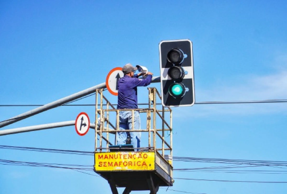 Trabalhador realiza manutenção em um semáforo utilizando plataforma elevada.