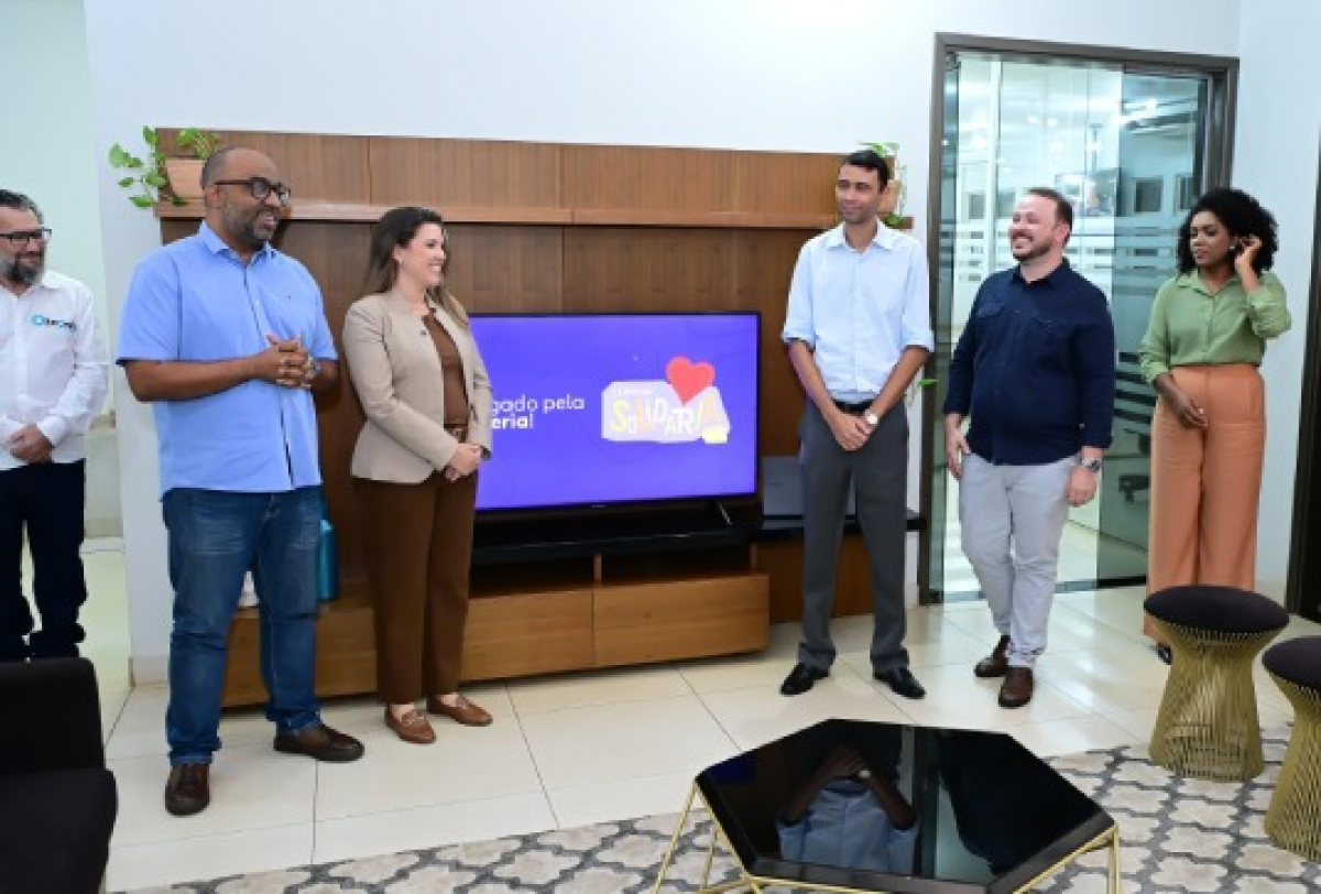 Grupo de pessoas reunido em ambiente corporativo durante apresentação ou evento informal.