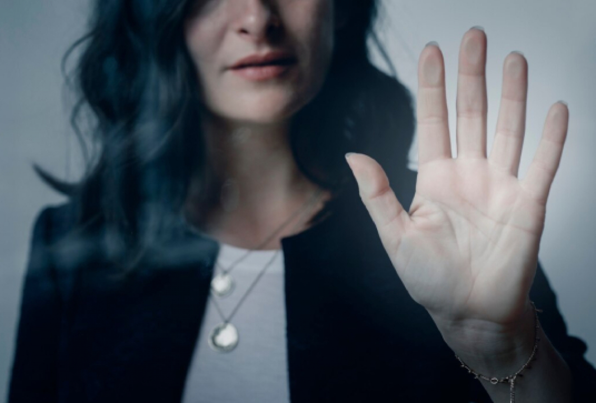 Mulher toca um vidro com expressão séria, transmitindo emoção e reflexão.