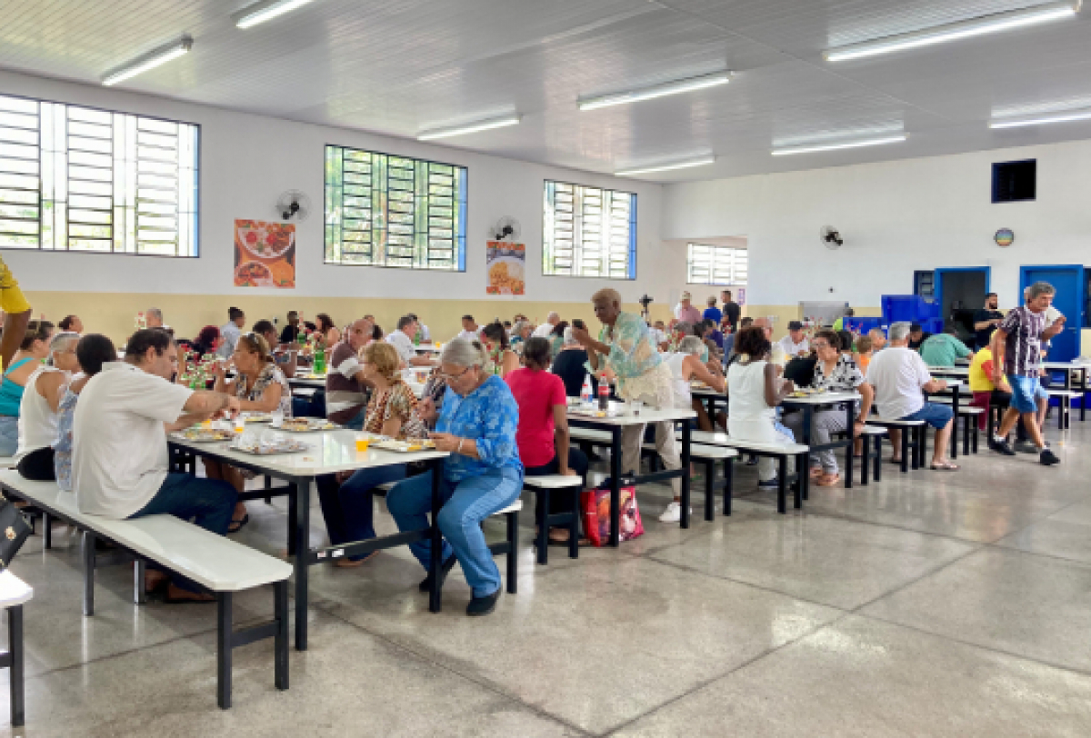 Pessoas almoçam em um restaurante popular movimentado, com ambiente iluminado e organizado.