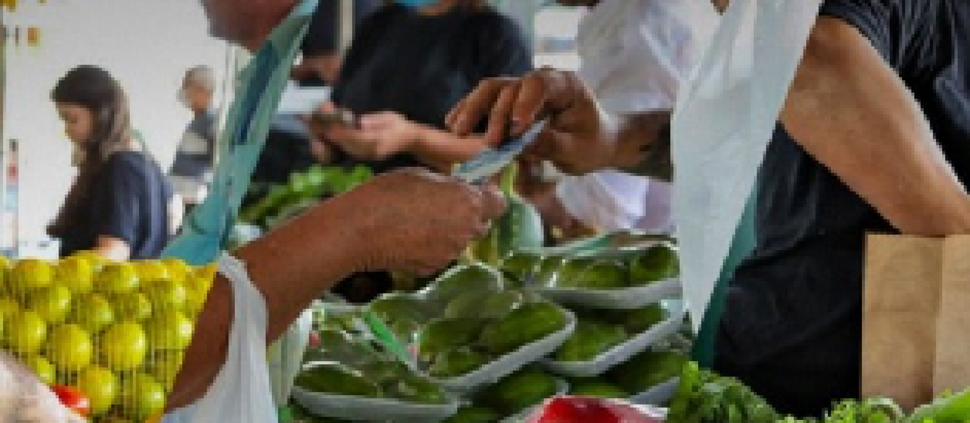 Cena de feira livre com venda de frutas e vegetais frescos sendo negociados entre clientes e vendedores.