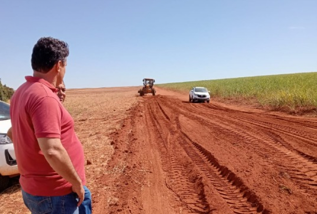 Cena rural mostra estrada de terra em obras, com máquinas e pessoas envolvidas em melhorias na infraestrutura local.