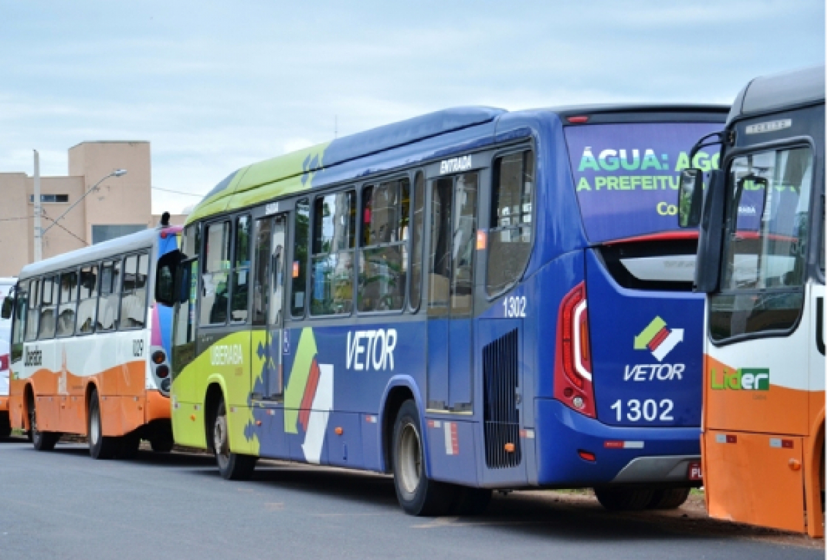 A imagem mostra uma fileira de ônibus estacionados na lateral de uma rua.