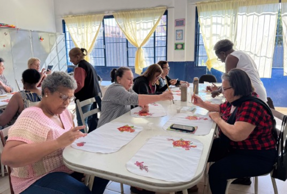 Mulheres participam de oficina de pintura em tecido em ambiente de convivência e aprendizado.