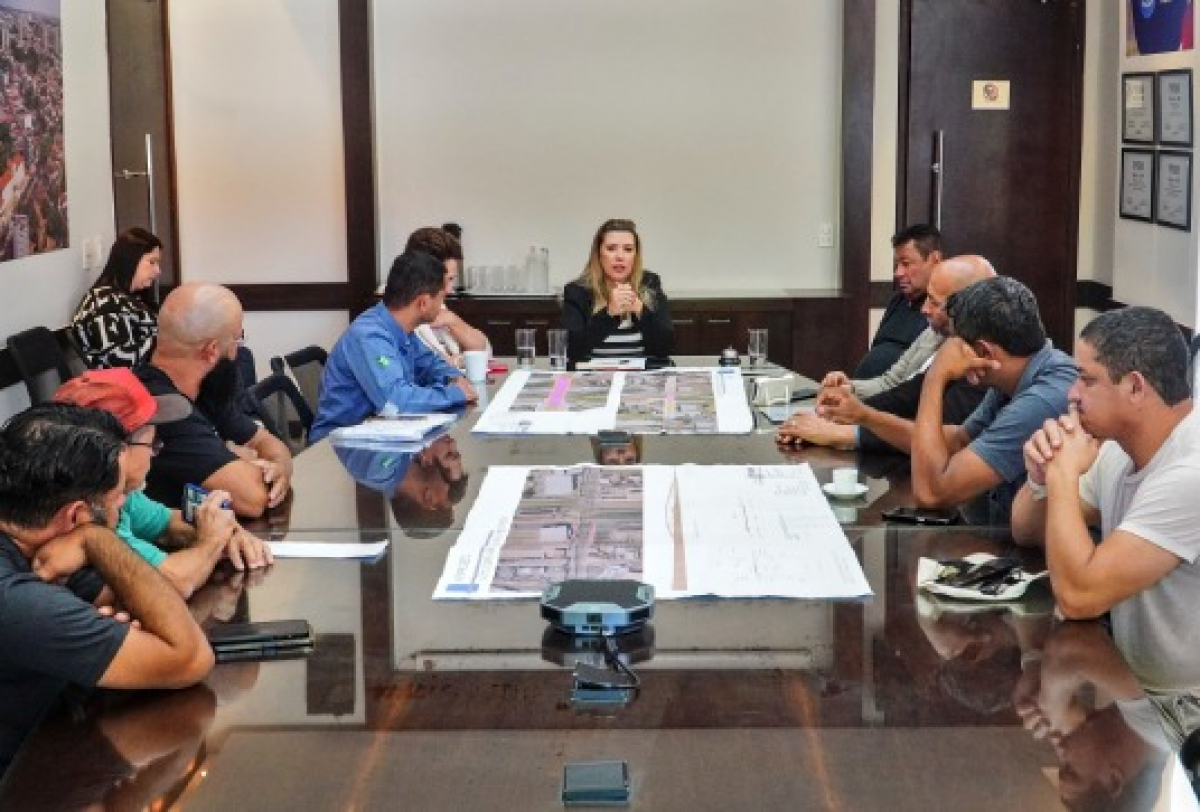 Reunião com vários participantes em torno de uma mesa discute projetos e plantas arquitetônicas.