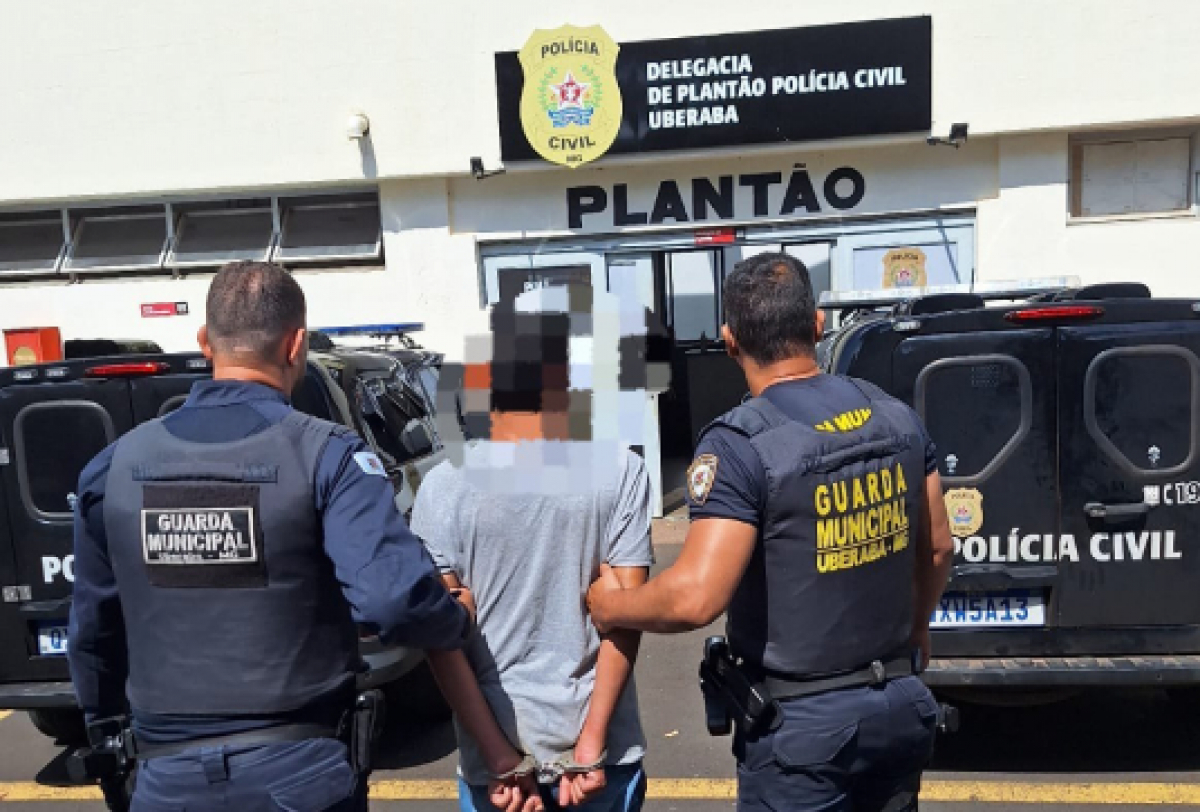 A imagem mostra dois guardas municipais escoltando uma pessoa algemada para uma delegacia. 