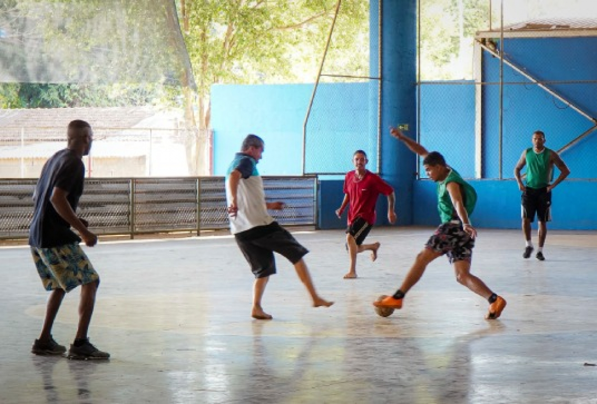 Grupo de homens joga partida de futsal em uma quadra coberta.
