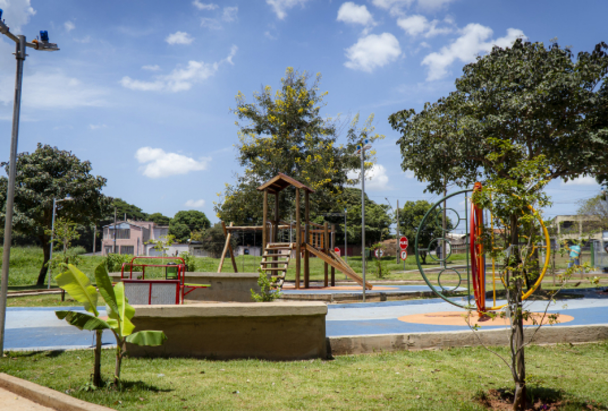 Um parquinho ao ar livre com brinquedos e área verde em um bairro residencial.