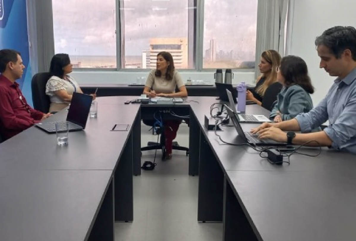 Reunião corporativa entre seis profissionais em ambiente de escritório com vista urbana.